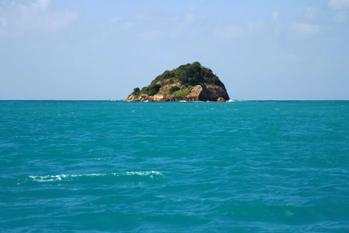 A small green islet rising from bright turquoise water off the coast of Antigua